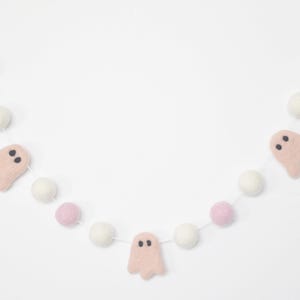May include: A pink and white felt garland with pink ghost cutouts. The garland is strung with white and pink pom poms.