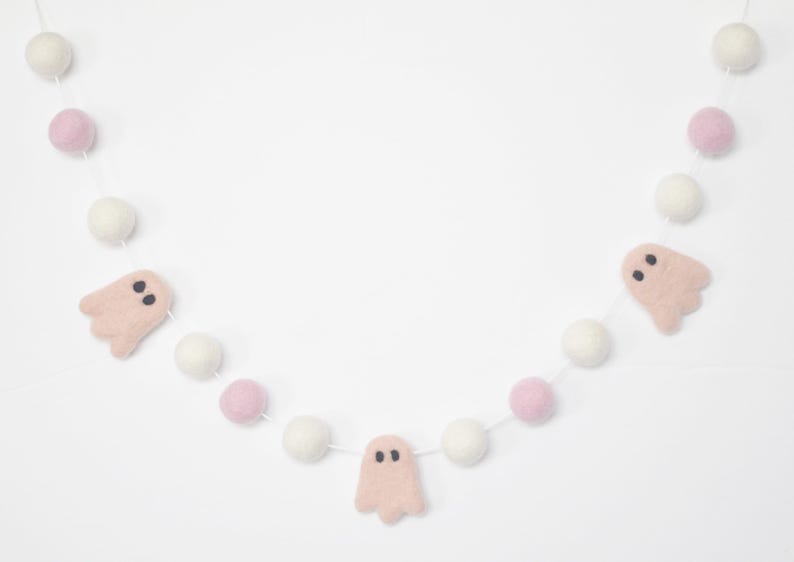 May include: A pink and white felt garland with pink ghost cutouts. The garland is strung with white and pink pom poms.