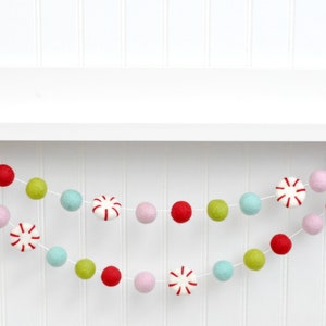 Felt peppermint garland with light pink, red, green, and aqua wool balls strung on a shelf.