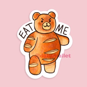 Op de afbeelding: Een bruine, beer-vormige broodsticker met de tekst "EAT ME" erop. De beer is getekend in een cartoon-stijl met een chagrijnige uitdrukking.