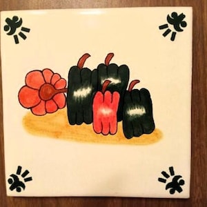 May include: A white ceramic tile with a hand-painted design of black and red peppers and a red flower. The tile has a black and white design in each corner.