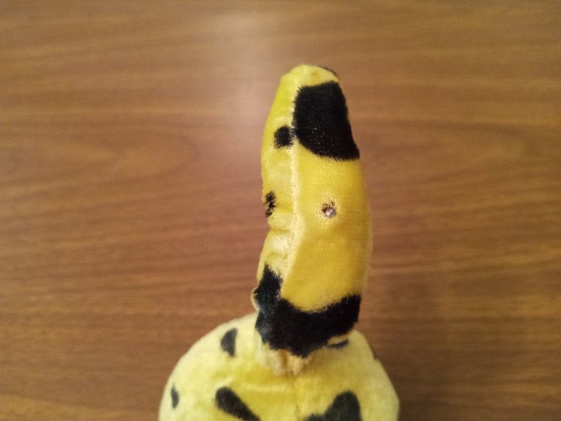 May include: A plush toy with a yellow body and black spots. The toy has a curved shape with a small, rounded head. The toy has two small, shiny embellishments on its head.