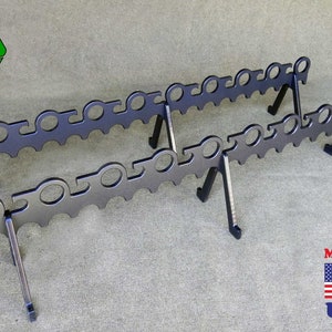 May include: Two black metal fire pit grates with a decorative design. The grates have a series of circular cutouts and are supported by angled legs. The image also includes a recycling symbol and a "Made in USA" graphic.