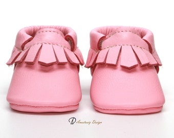 May include: A pair of pink leather baby moccasins with fringe detailing.