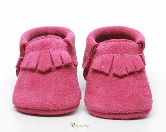 May include: A pair of pink suede baby moccasins with fringe detail. The moccasins have a soft, comfortable fit and are perfect for little feet.