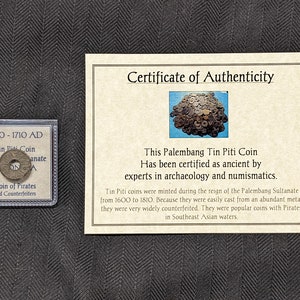 Op de afbeelding: Een certificaat van echtheid voor een Palembang Tin Piti-munt, gedateerd 1600-1710 na Christus. Het certificaat stelt dat de munt is gecertificeerd als oud door experts in archeologie en numismatiek. Het certificaat bevat ook een klein beeld van een stapel munten en een close-up van de munt.