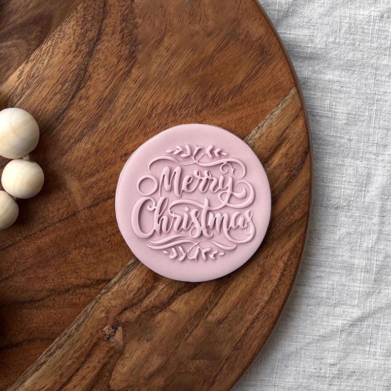 Plastic cookie cutter and fondant stamp with a custom design saying "Merry Christmas", made of durable plastic and shown on a countertop.