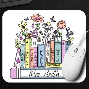May include: White mousepad with a floral and book design. The mousepad features colorful flowers and books with words like "Teach", "Love", and "Inspire". The name "Mrs. Smith" is written at the bottom.