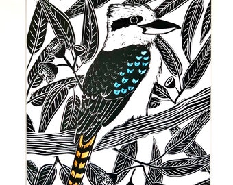 Puede incluir: Una impresión de linóleo en blanco y negro de un kookaburra posado en una rama con hojas de eucalipto. El pájaro tiene marcas azules y amarillas.