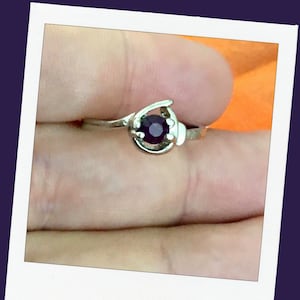 May include: A silver ring with a single, round, dark purple gemstone set in a prong setting.