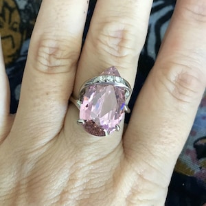 May include: A silver ring featuring a large pink pear-shaped gemstone and smaller clear gemstones set in a silver band.