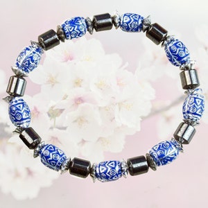 Könnte beinhalten: Ein blaues und silbernes Armband mit geometrischen Mustern auf den Perlen. Das Armband besteht aus Hämatit- und Keramikperlen.