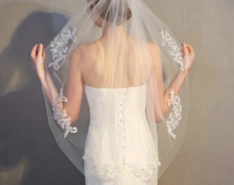 May include: A white bridal veil with delicate lace trim. The veil is made of soft tulle and has a single layer.