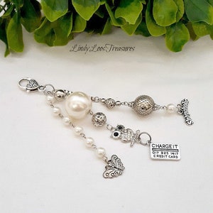 以下が含まれることがあります： 大きな白い真珠、銀製のフクロウのチャーム、蝶のチャーム、そして「CHARGE IT」クレジットカードのチャームが付いた銀製のチャームブレスレット。ブレスレットには、銀製の留め具と銀製の「Shopalcoholic」チャームも付いています。