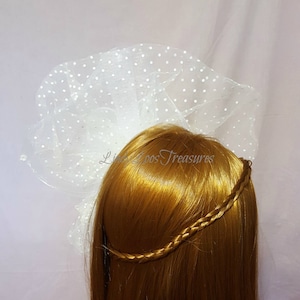 Op de afbeelding: Wit tule sluier met stippen, gedragen op een blond pruik met een gevlochten hoofdband.