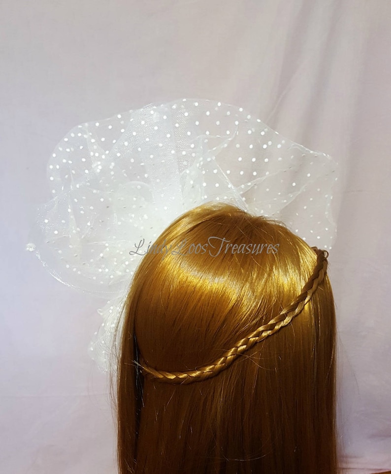 Op de afbeelding: Wit tule sluier met stippen, gedragen op een blond pruik met een gevlochten hoofdband.