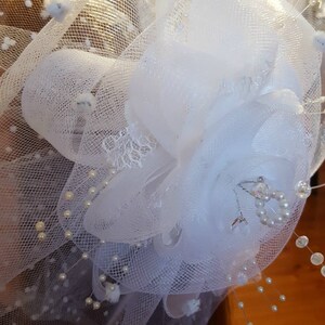 Op de afbeelding: Witte tule bloem met parel accenten en een klein stukje kant. De bloem is gemaakt van meerdere lagen tule en is versierd met kleine witte parels. De bloem is bevestigd aan een wit tule sluier.