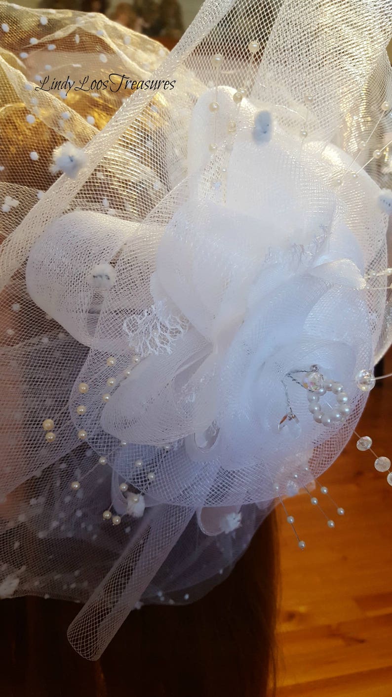 Op de afbeelding: Witte tule bloem met parel accenten en een klein stukje kant. De bloem is gemaakt van meerdere lagen tule en is versierd met kleine witte parels. De bloem is bevestigd aan een wit tule sluier.