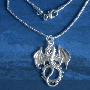 Op de afbeelding: Een zilveren ketting met een zilveren drakenhanger. De draak bevindt zich in een vliegende pose met uitgespreide vleugels.