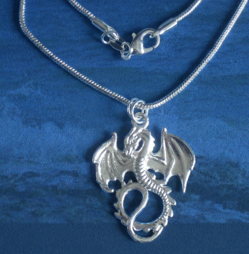 Op de afbeelding: Een zilveren ketting met een zilveren drakenhanger. De draak bevindt zich in een vliegende pose met uitgespreide vleugels.