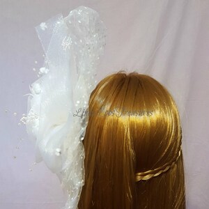 Op de afbeelding: Wit tule haaraccessoire met parel accenten. De tule is gebundeld en gelaagd om een volumineuze look te cre&euml;ren. Het accessoire is bevestigd aan een haar kam.