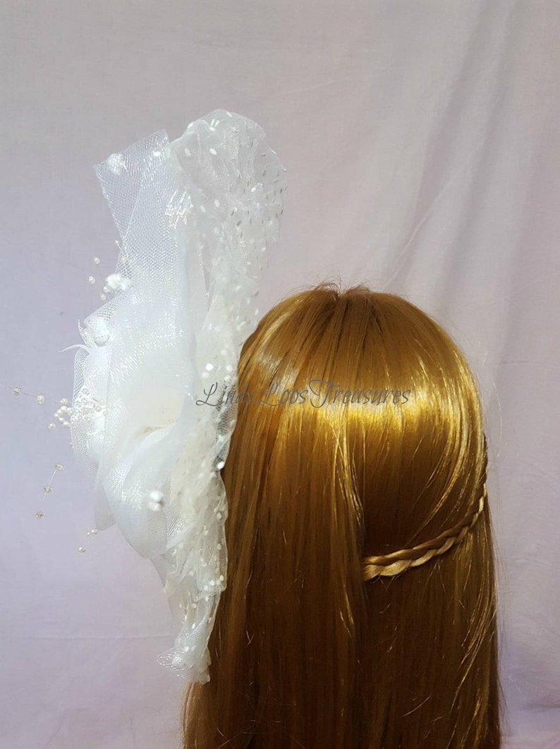 Op de afbeelding: Wit tule haaraccessoire met parel accenten. De tule is gebundeld en gelaagd om een volumineuze look te cre&euml;ren. Het accessoire is bevestigd aan een haar kam.