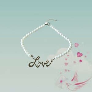Puede incluir: Un collar de perlas blancas con un colgante de plata que dice "Love".