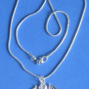 Op de afbeelding: Een zilveren ketting met een zilveren drakenhanger. De draak bevindt zich in een vliegende pose met uitgespreide vleugels.