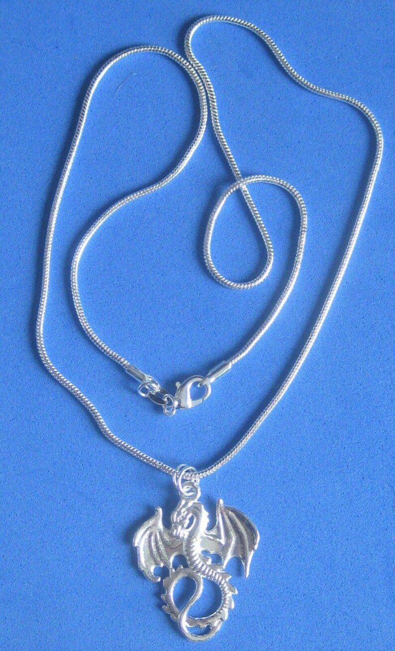 Op de afbeelding: Een zilveren ketting met een zilveren drakenhanger. De draak bevindt zich in een vliegende pose met uitgespreide vleugels.