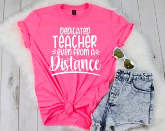 Może przedstawiać: Różowy T-shirt z napisem "Dedicated Teacher Even From A Distance" w białym kolorze.