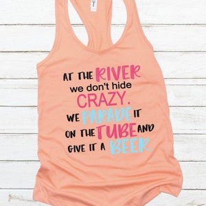 May include: Peach-colored tank top with a black graphic that reads "At the river we don't hide crazy. We parade it on the tube and give it a beer."