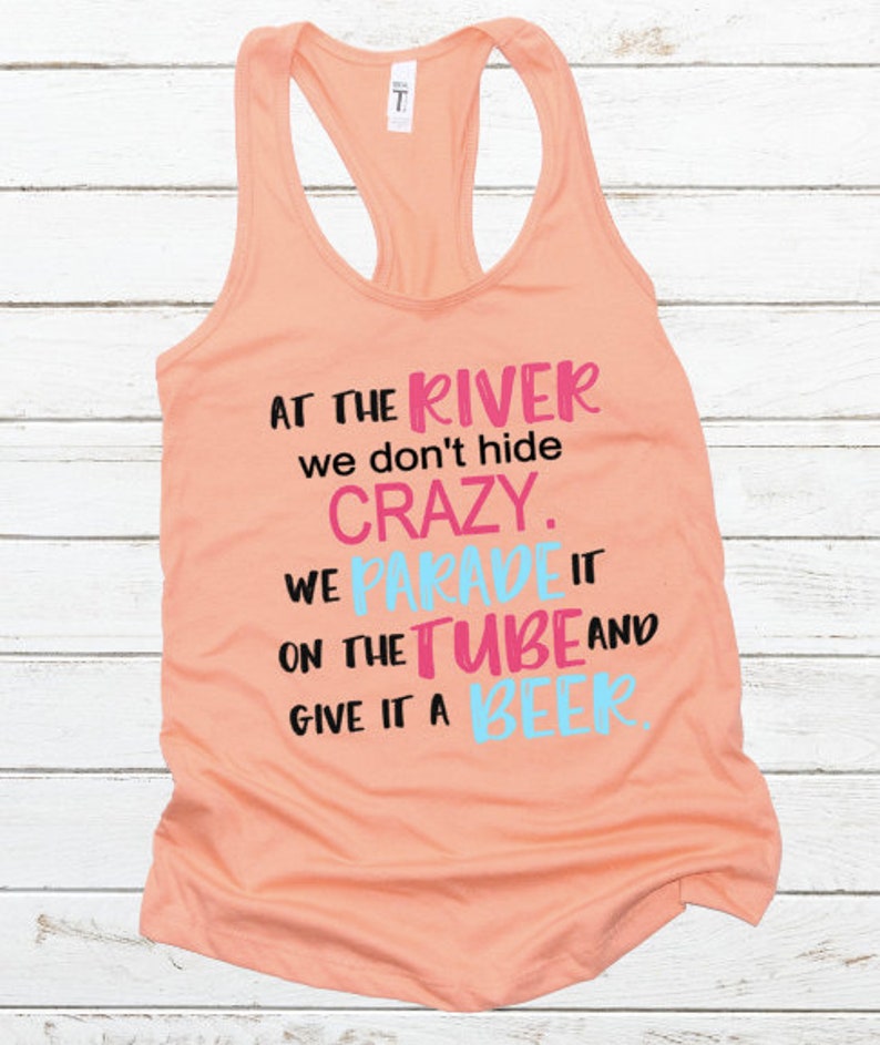 May include: Peach-colored tank top with a black graphic that reads "At the river we don't hide crazy. We parade it on the tube and give it a beer."