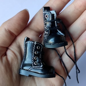 May include: A pair of black leather doll boots with white stitching and black laces. The boots have a round toe and a chunky heel.