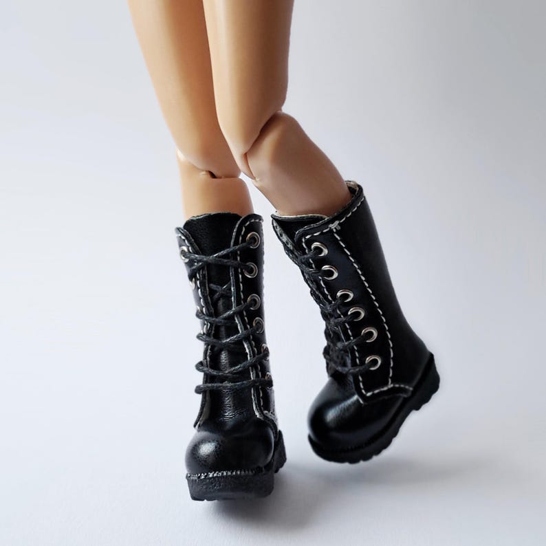 K&ouml;nnte beinhalten: Schwarze Puppenstiefel mit Schn&uuml;rsenkeln und silbernen &Ouml;sen. Die Stiefel haben eine runde Spitze und einen kleinen Absatz. Die Stiefel sind aus gl&auml;nzendem Material gefertigt und haben wei&szlig;e N&auml;hte an den R&auml;ndern.