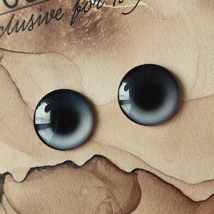 May include: Two black and white glass eyes with a black pupil and a white ring around the pupil. The eyes are on a brown surface.