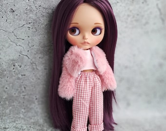 May include: A doll with long, straight dark purple hair, brown eyes, and purple eyeshadow. The doll wears a light pink cropped top, a fluffy light pink faux fur jacket, pink and white gingham trousers with cuffed hems, and white shoes.