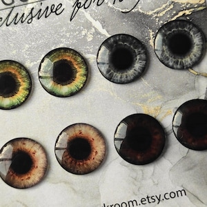 May include: Set of ten colorful glass eyes with black pupils. The eyes are arranged in two rows of five. The eyes are all different colors, including green, brown, and gray.