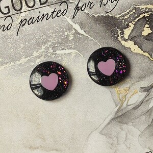 May include: A pair of black stud earrings with pink glitter and a pink heart in the center.