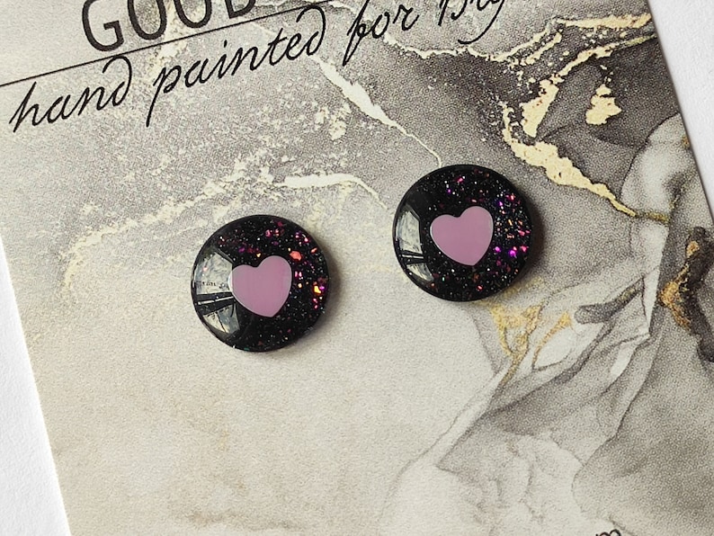 May include: A pair of black stud earrings with pink glitter and a pink heart in the center.