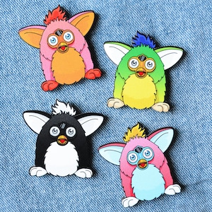 Könnte beinhalten: Vier bunte, flauschige Spielzeugnadeln mit unterschiedlich farbigem Fell und Augen. Die Spielzeuge sind in Form eines kleinen Tieres mit großen Augen und einem kleinen Mund gestaltet. Die Spielzeuge sind alle in verschiedenen Farben: orange, grün, schwarz und rosa.