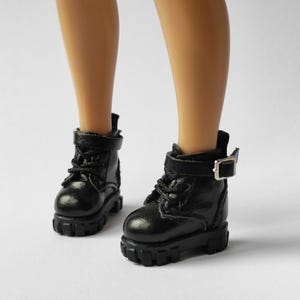 May include: Black leather ankle boots with buckles and laces. The boots have a chunky sole and are made for dolls.