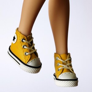May include: A pair of yellow high-top sneakers with white laces and a white toe cap. The sneakers have a black and white stripe around the sole and a white star on the side. The shoes are on a white background.