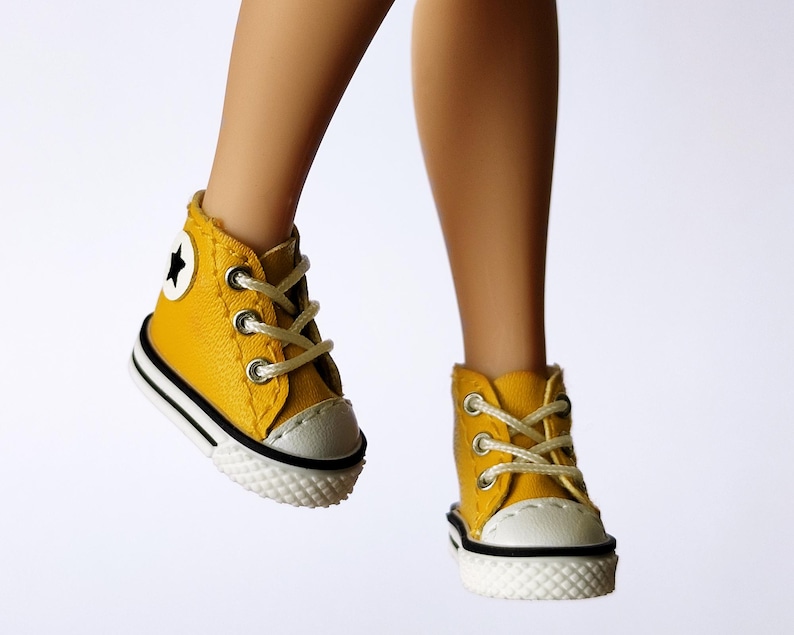 May include: A pair of yellow high-top sneakers with white laces and a white toe cap. The sneakers have a black and white stripe around the sole and a white star on the side. The shoes are on a white background.