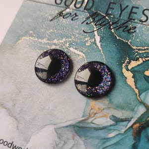May include: Two black plastic eyes with iridescent glitter. The eyes are round and have a black center. The eyes are on a blue and white background with the text "GOOD EYES for Blythe".
