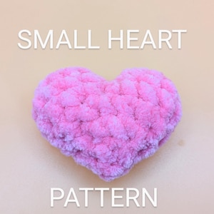 May include: A pink crocheted heart shaped pillow with the text "SMALL HEART PATTERN" on a light beige background.