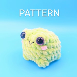 May include: A green crocheted frog plush toy with black eyes and a pink tongue. The frog is sitting on a light blue background. The word "PATTERN" is written in white above the frog.