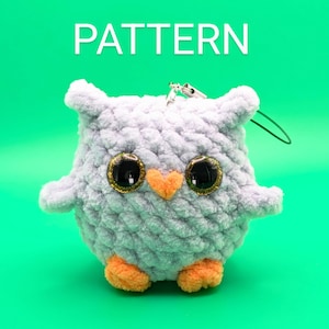 May include: A crocheted owl plush toy with large, glittery eyes and orange feet. The owl is light purple and has a textured, fluffy surface.