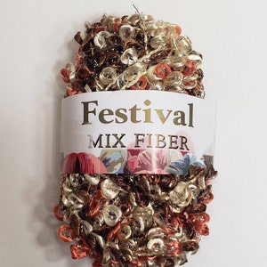 May include: A skein of Festival Mix Fiber yarn in shades of brown, gold, and orange. The yarn has a looped texture and a label with the word "Festival" in gold lettering.