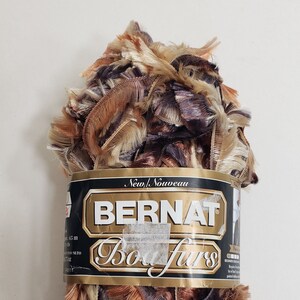 Può includere: Un gomitolo di filato Bernat Boa Fur in una miscela di tonalità marroni, beige e viola. Il filato è in pelliccia sintetica ed è progettato per la maglia e l'uncinetto.