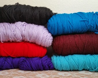 May include: A stack of six skeins of yarn in various colors, including black, lavender, red, purple, turquoise, and a darker blue.